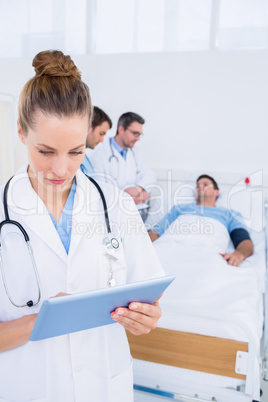 Doctor using digital tablet with colleagues and patient behind