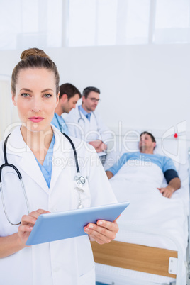 Doctor using digital tablet with colleagues and patient behind