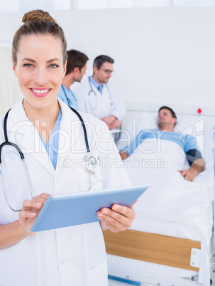 Doctor using digital tablet with colleagues and patient behind