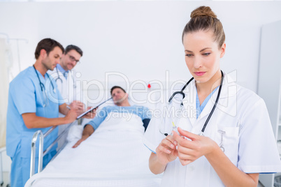 Doctor holding syringe with colleagues and patient at hospital