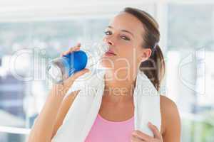 Woman with towel drinking water in gym