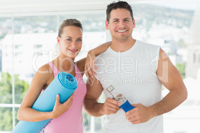 Fit couple holding water bottle and exercise mat in exercise roo