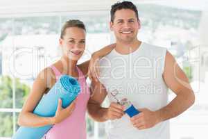 Fit couple holding water bottle and exercise mat in exercise roo