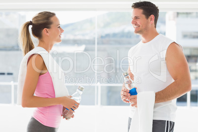 Fit couple holding water bottles and towels in exercise room