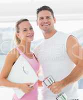 Fit couple holding dumbbell and weighing scale