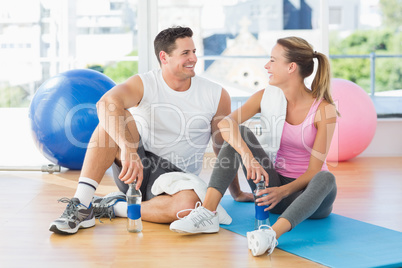 Young couple with water bottles chatting at gym