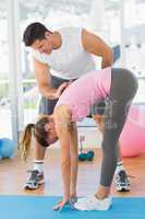 Male trainer assisting young woman with pilate exercises