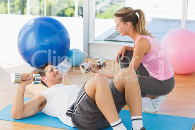 Female trainer looking at young man exercise in gym