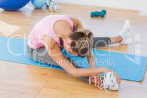 Sporty woman stretching hand to leg in fitness studio