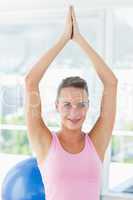 Smiling woman with joined hands over head at fitness studio