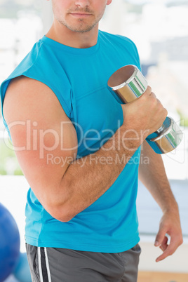 Mid section of a sporty man with dumbbell in gym