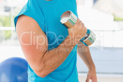 Mid section of a sporty man with dumbbell in gym