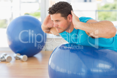 Young man exercising on fitness ball at a bright gym