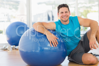 Smiling young man sitting with fitness ball at gym