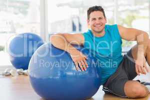 Smiling young man sitting with fitness ball at gym