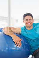 Smiling young man sitting with fitness ball at gym