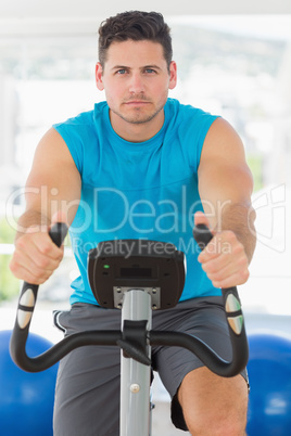 Serious young man working out at spinning class