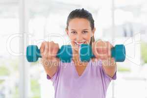 Smiling young woman lifting dumbbell weights