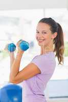 Side view of a smiling woman lifting dumbbell weights