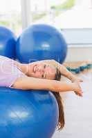 Smiling fit woman lying on exercise ball at gym