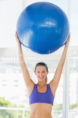 Smiling fit young woman holding up fitness ball