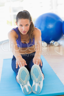 Sporty woman stretching hands to legs in fitness studio