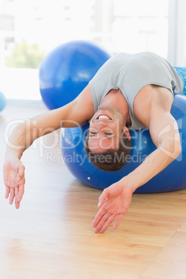 Happy fit man stretching on exercise ball at gym