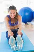 Sporty young woman stretching hands to legs in fitness studio