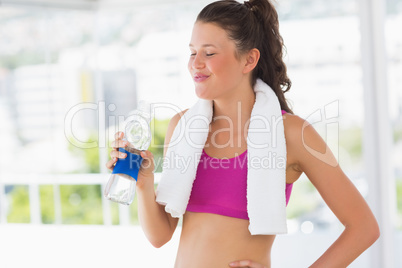 Fit woman with towel drinking water in gym