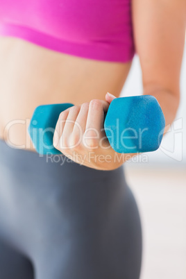 Mid section of a woman lifting dumbbell weight