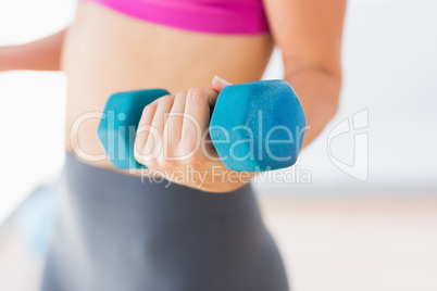 Mid section of a woman lifting dumbbell weight in gym