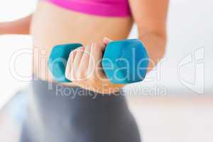 Mid section of a woman lifting dumbbell weight in gym