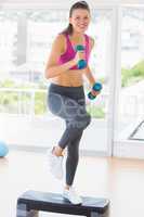 Fit woman performing step aerobics exercise with dumbbells
