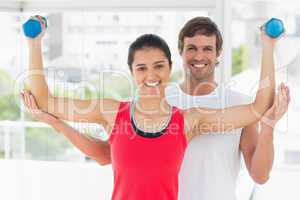 Smiling instructor with woman lifting dumbbell weights