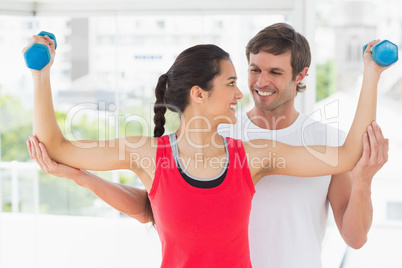Smiling instructor with woman lifting dumbbell weights