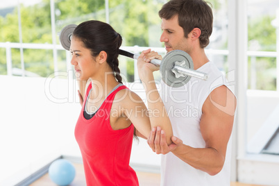 Male trainer helping fit woman to lift the barbell