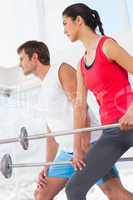Fit young couple holding barbells in the gym