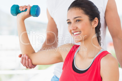 Instructor assisting smiling woman with dumbbell weight