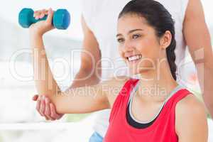 Instructor assisting smiling woman with dumbbell weight