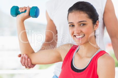 Instructor assisting smiling woman with dumbbell weight