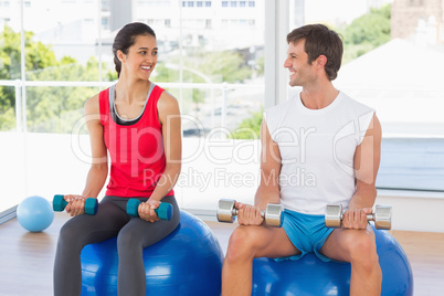 Happy couple lifting dumbbells while sitting on fitness balls in