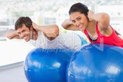 Fit couple exercising on fitness balls in gym