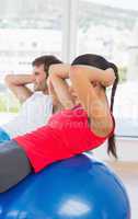 Fit young couple exercising on fitness balls in gym
