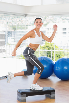 Fit young woman performing step aerobics exercise