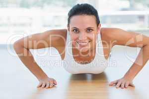 Smiling beautiful woman doing push ups in gym