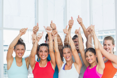 Fit people gesturing thumbs up in exercise room