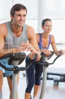 Smiling young couple working out at spinning class