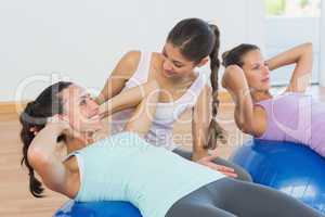 Trainer helping young woman with fitness ball