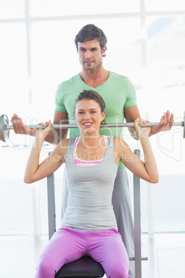 Trainer helping fit woman to lift barbell bench press