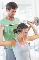 Trainer helping fit woman to lift barbell bench press